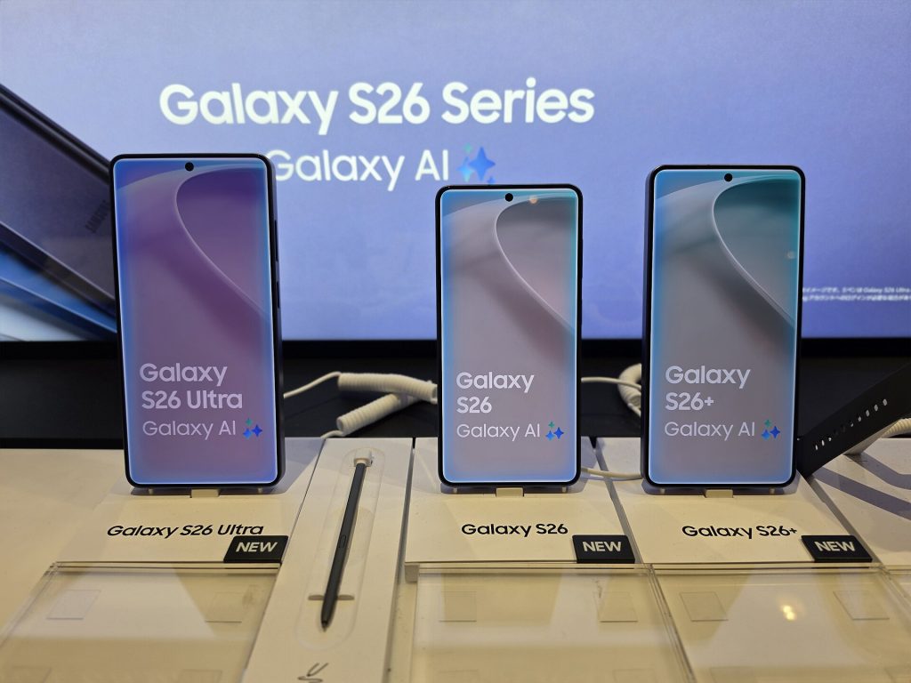 ثلاث جوالات Galaxy S26 Ultra و S26 و S26+ على منصة عرض وخلفها شاشة مكتوب عليها Galaxy AI